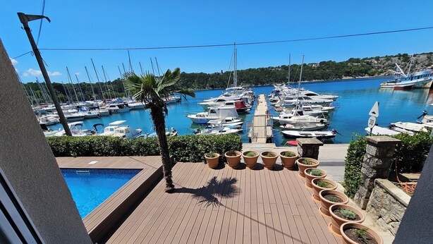 A view from a balcony overlooking a marina with boats docked, a swimming pool, and potted plants. - Villa Gaj (Omisalj)