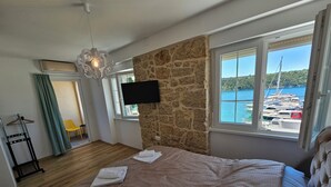 A bedroom with a large bed, a stone wall, a TV, and a view of boats and water. - Villa Gaj (Omisalj)