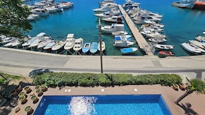 A marina with various boats docked, a swimming pool with a wooden deck, and a view of the surrounding water and greenery. - Villa Gaj (Omisalj)