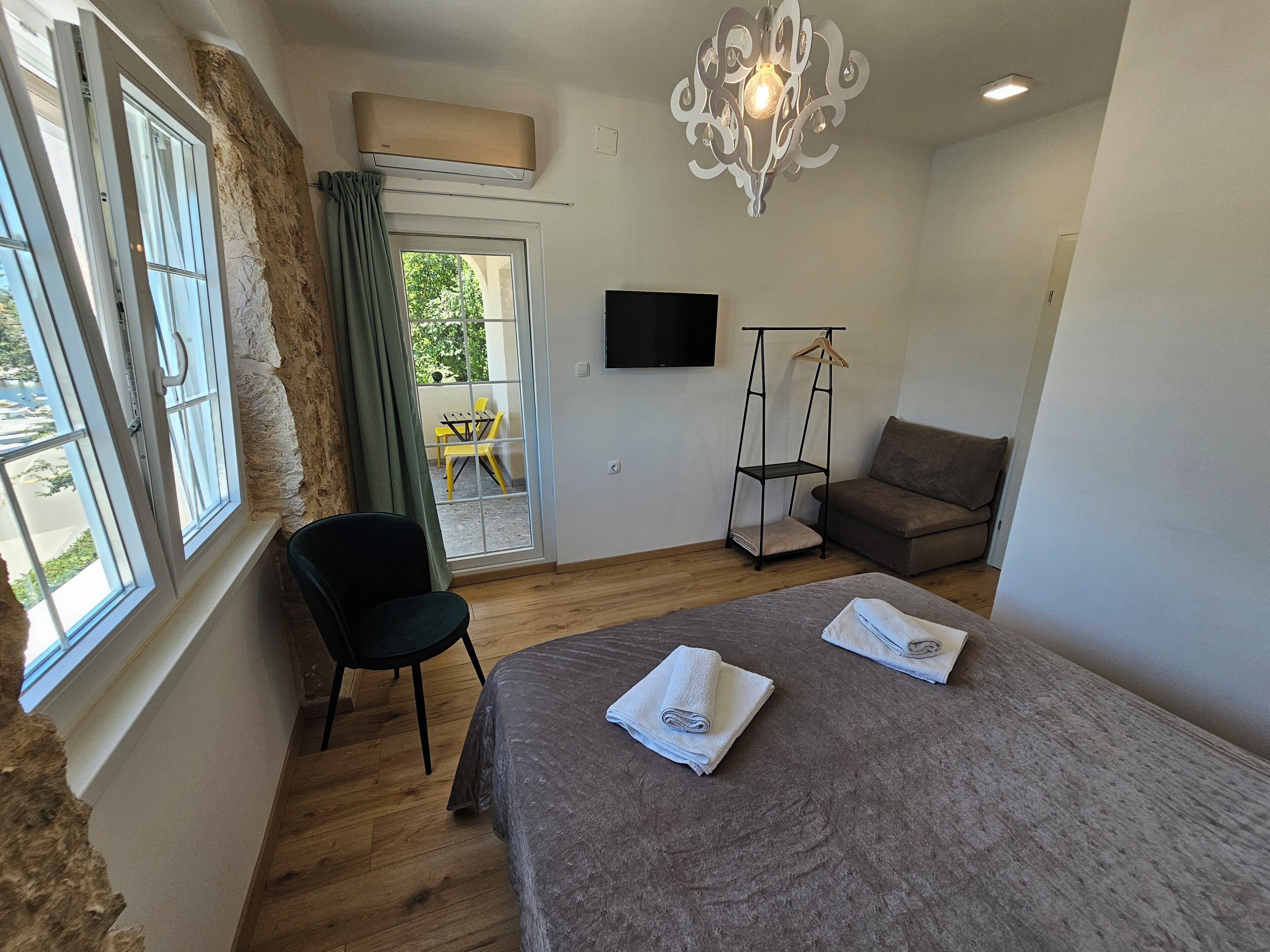 A room with a bed, a chair, a sofa, a TV, and a window with curtains.