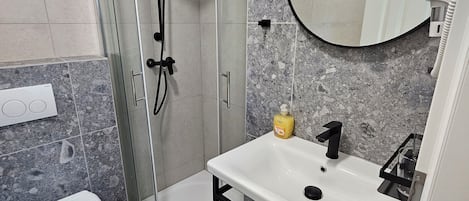 A modern bathroom with a glass-enclosed shower, a white sink with a black faucet, and a marble-tiled floor.