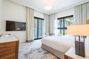 Une chambre d’hôtel avec un grand lit, un téléviseur à écran plat, un bureau et une vue sur les palmiers par les fenêtres.