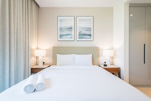 A hotel room with a large bed, two bedside tables with lamps, a wooden nightstand, and a door. - Seafront 4BR Apartment with Assistant Room in The Address Fujairah Residences Block B, Fujairah (Fujairah)