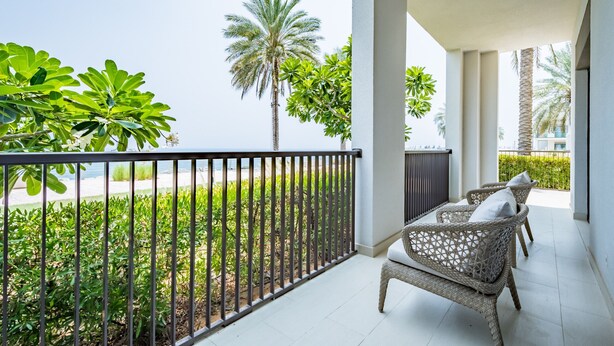 A balcony with a view of the sea, featuring wicker furniture and a palm tree.