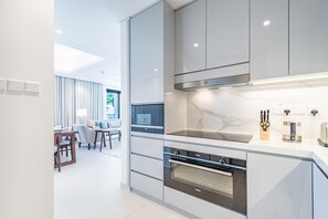 A modern kitchen with integrated appliances, a dining area with a sofa and table, and a view of the living room. - Seafront 4BR Apartment with Assistant Room in The Address Fujairah Residences Block B, Fujairah (Fujairah)