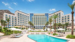 A hotel with a swimming pool, palm trees, and a mountainous backdrop.