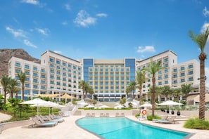 A hotel with a swimming pool, palm trees, and a mountainous backdrop. - Seafront 4BR Apartment with Assistant Room in The Address Fujairah Residences Block B, Fujairah (Fujairah)