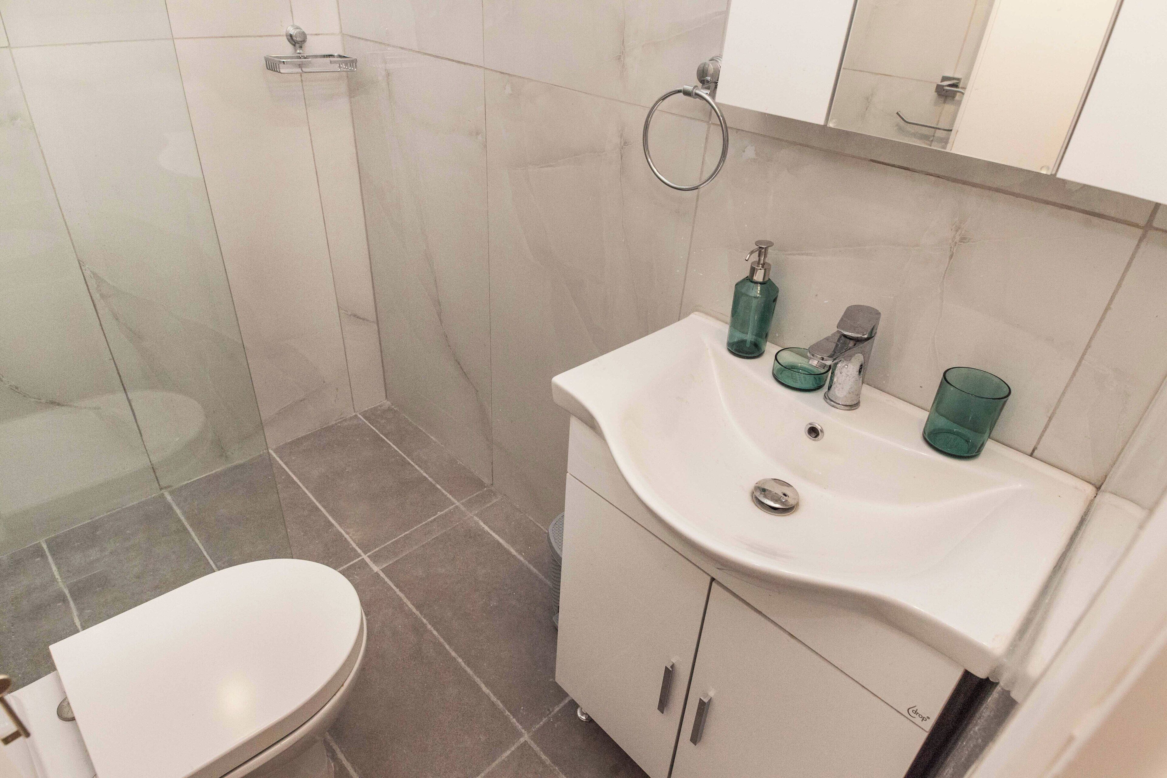 A bathroom with a toilet, a sink with a mirror above it, and a shower area.