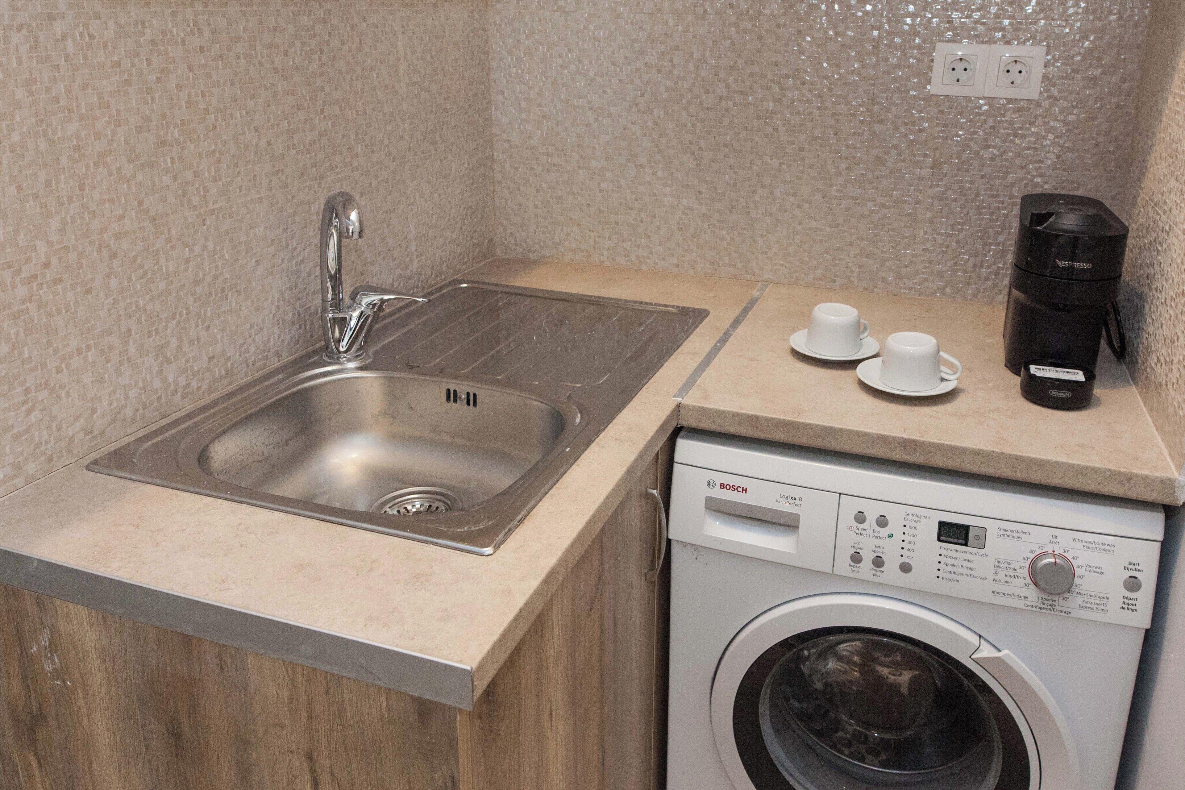 A compact kitchen with a stainless steel sink, a Bosch washing machine, and a coffee maker.
