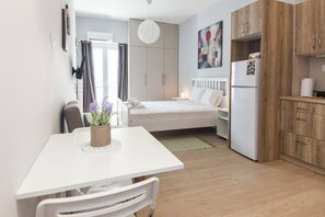 A compact room with a bed, a small kitchenette, a dining table with chairs, and a potted plant. - Fresh Exarcheia Studio w Balcony & Style (Athens)