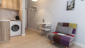 Un espace de vie compact comprenant un lave-linge, une petite table à manger avec des chaises et un canapé coloré.