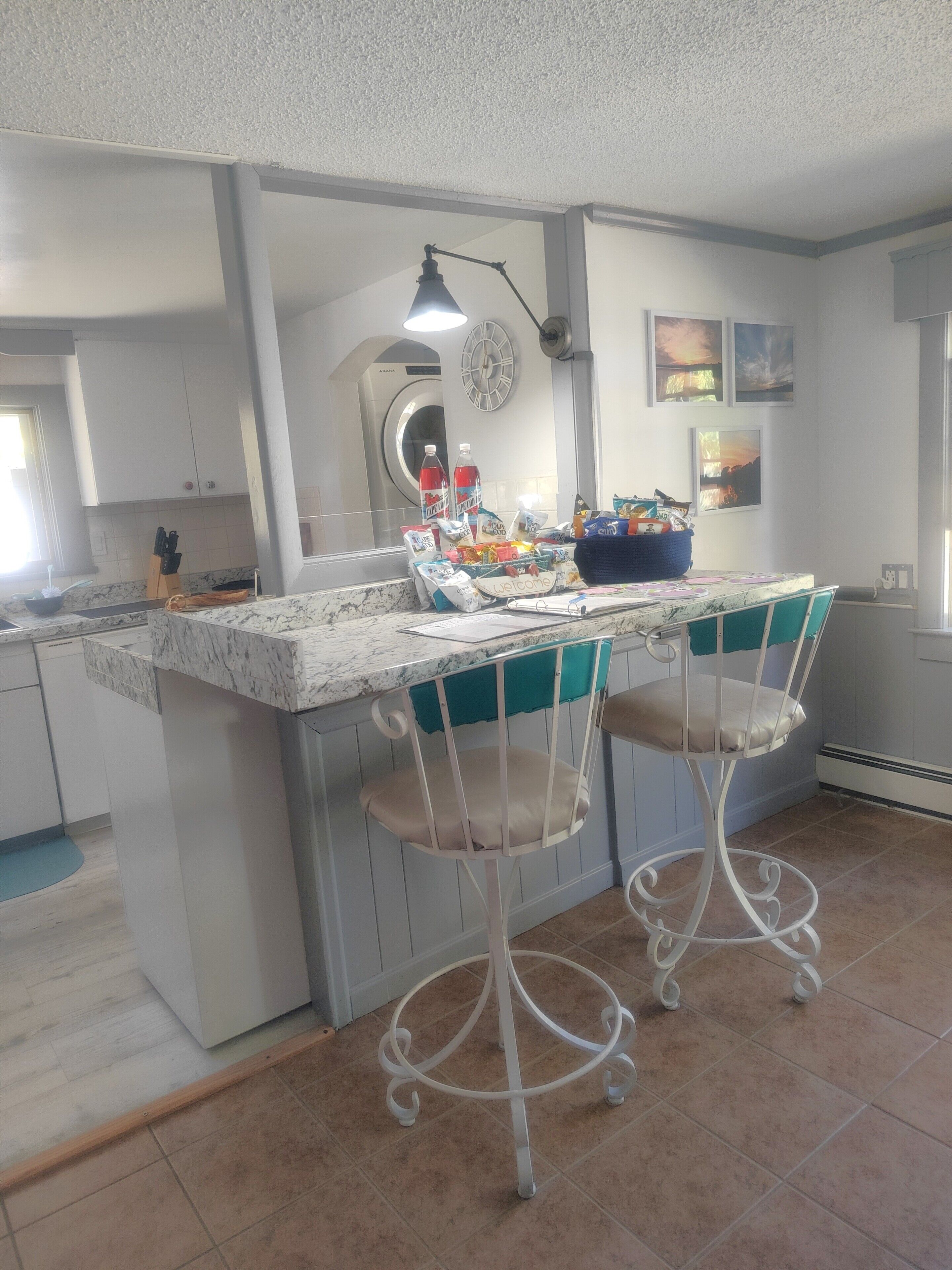 Een keuken met een marmeren aanrecht, twee witte barstoelen, een spoelbak en een klok aan de muur.