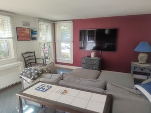 Uma sala de estar com sofá, televisão, luminária e mesa com jogos de tabuleiro.