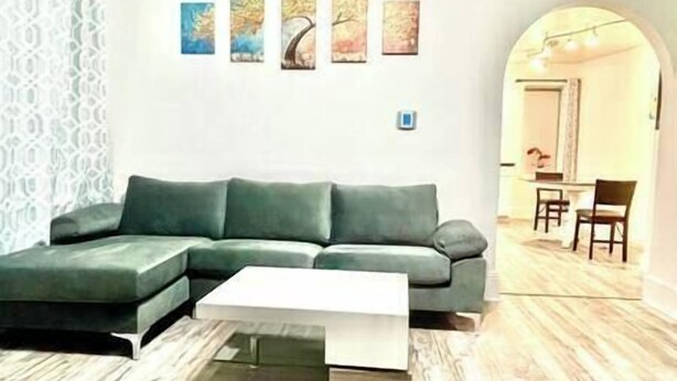 Una sala de estar moderna con un sofá seccional verde, una mesa de centro blanca y un comedor con mesa y sillas.