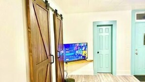 Una habitación con puerta corredera de madera, televisor de pantalla plana montado y puerta verde azulado al fondo.