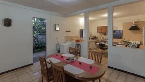 Un coin repas avec une table dressée pour quatre personnes, une cuisine en arrière-plan et une vue sur l’extérieur.