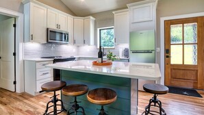A modern kitchen with white cabinets, a central island with stools, a microwave, and a refrigerator.