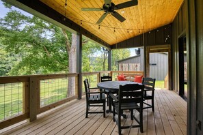 A covered outdoor deck with a table and chairs, a ceiling fan, and a view of a grassy area. - Still Waters on Watauga River (Johnson City)