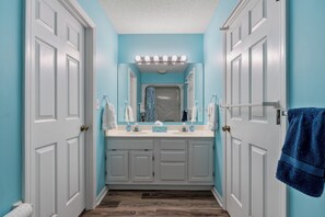 A bathroom with two white doors, a blue wall, a white vanity with a mirror, and a blue towel hanging on the right. - 5-Bedroom Large Home in Windy Hill -Jus' Yungins (North Myrtle Beach)