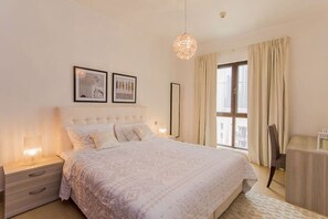 A bedroom with a bed, nightstands, a desk, a hanging light fixture, and two framed pictures on the wall.