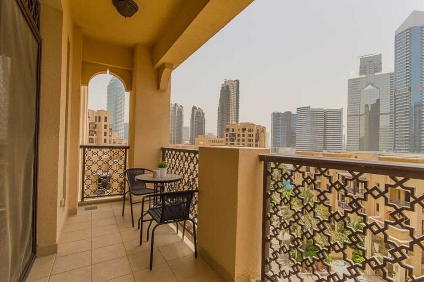 Un balcone con vista sulla città, un tavolino con sedie e una ringhiera decorativa.