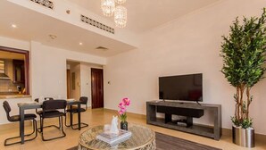 A modern living room with a dining area, a flat-screen TV, and a potted plant. - Walking Distance to Burj Khalifa! (Old Town Dubai)