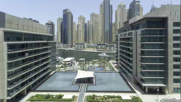 A high-rise building with multiple floors, a central courtyard with a water feature, and a marina in the background.