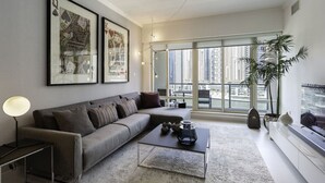 A modern living room with a grey sofa, a coffee table, and a large window offering a view of high-rise buildings.