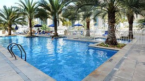 A swimming pool with a metal ladder, surrounded by palm trees and a white fence.