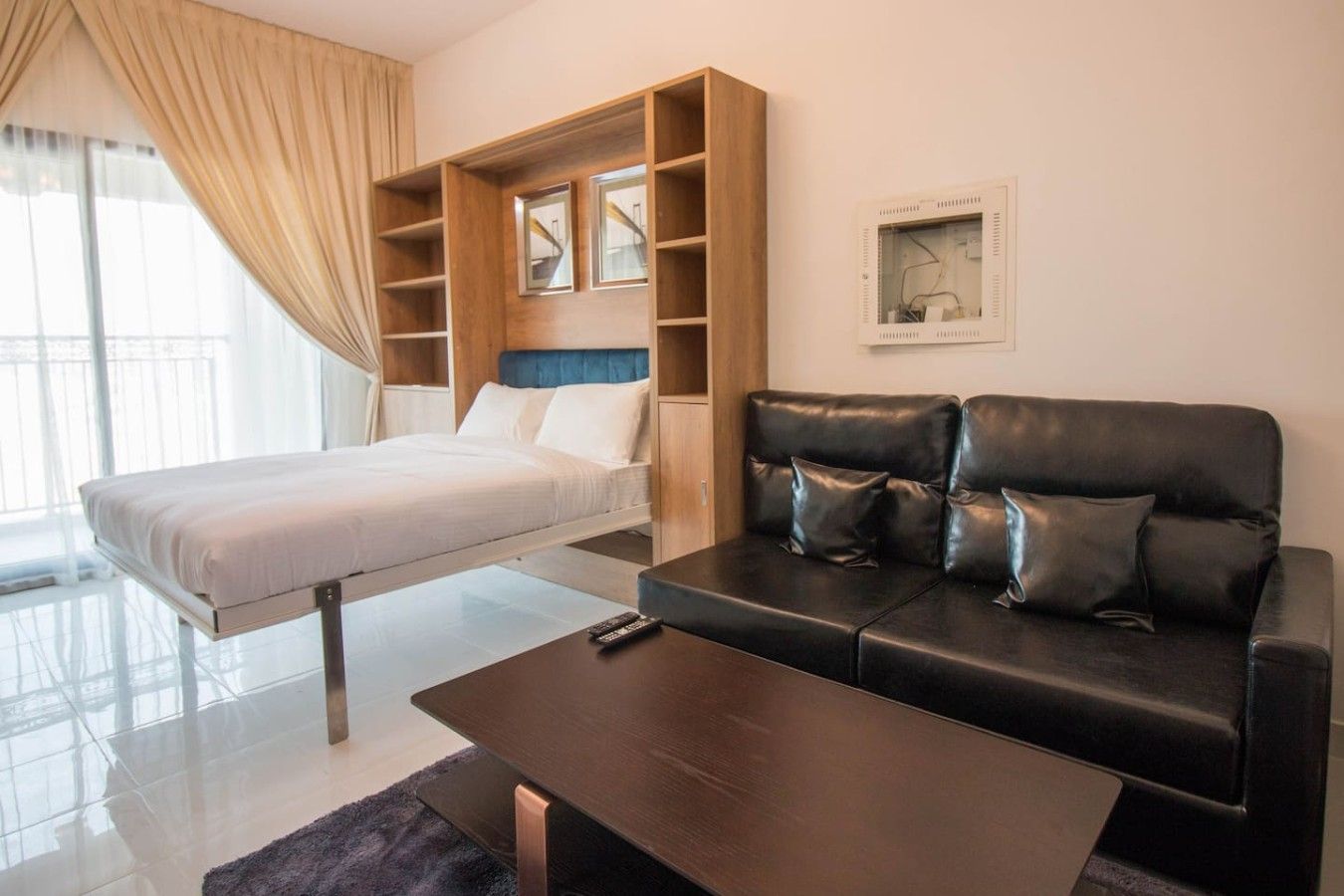 A modern hotel room with a bed, a sofa, a coffee table, and a built-in shelving unit.
