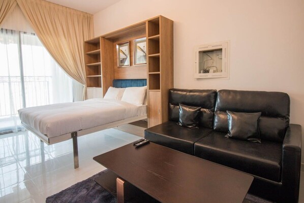 A modern hotel room with a bed, a sofa, a coffee table, and a built-in shelving unit.