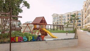Ein Spielplatz mit Rutsche und Klettergerüsten, umgeben von einem Gebäude mit mehreren Balkonen und einer gepflegten Grünfläche.