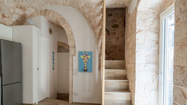 Une cuisine équipée d’un réfrigérateur moderne, d’un escalier en bois et ornée d’un tableau décoratif au mur.