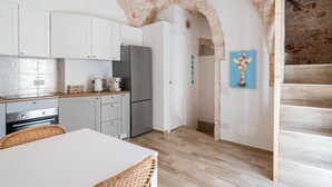 Une cuisine moderne avec des meubles blancs, un réfrigérateur en acier inoxydable et un coin repas comprenant une table blanche et des chaises en osier.