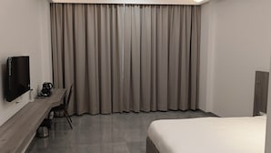 Ένα δωμάτιο ξενοδοχείου με ένα κρεβάτι, ένα γραφείο με τηλεόραση και ένα μεγάλο παράθυρο με κουρτίνες.