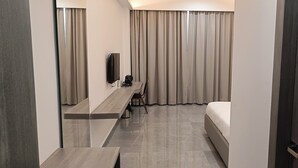 Ένα δωμάτιο ξενοδοχείου με ένα κρεβάτι, ένα γραφείο με καρέκλα, μια τηλεόραση και κουρτίνες.