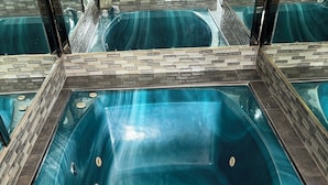 A rectangular hot tub with a clear blue interior, surrounded by a tiled border and a brick pattern wall. - LUXURY INN (Houston)