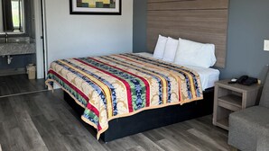 A bedroom with a large bed, a headboard, a bedside table with a phone, and a chair. - LUXURY INN (Houston)