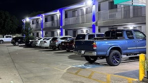 A parking lot with several parked vehicles, including a blue pickup truck and a white sedan. - LUXURY INN (Houston)