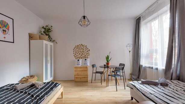 Una habitación compacta con dos camas, una mesa de comedor, sillas, un mueble pequeño y una planta en maceta.