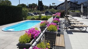 En swimmingpool omgiven av blomsterrabatter, utomhusmöbler och en modern byggnad i bakgrunden.