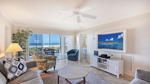A living room with a TV, sofa, armchair, and a view of the beach. - Dramatic Siesta Key Gulf Views 3 Bed 3 Bath Top Floor Steps to Beach (Siesta Key)