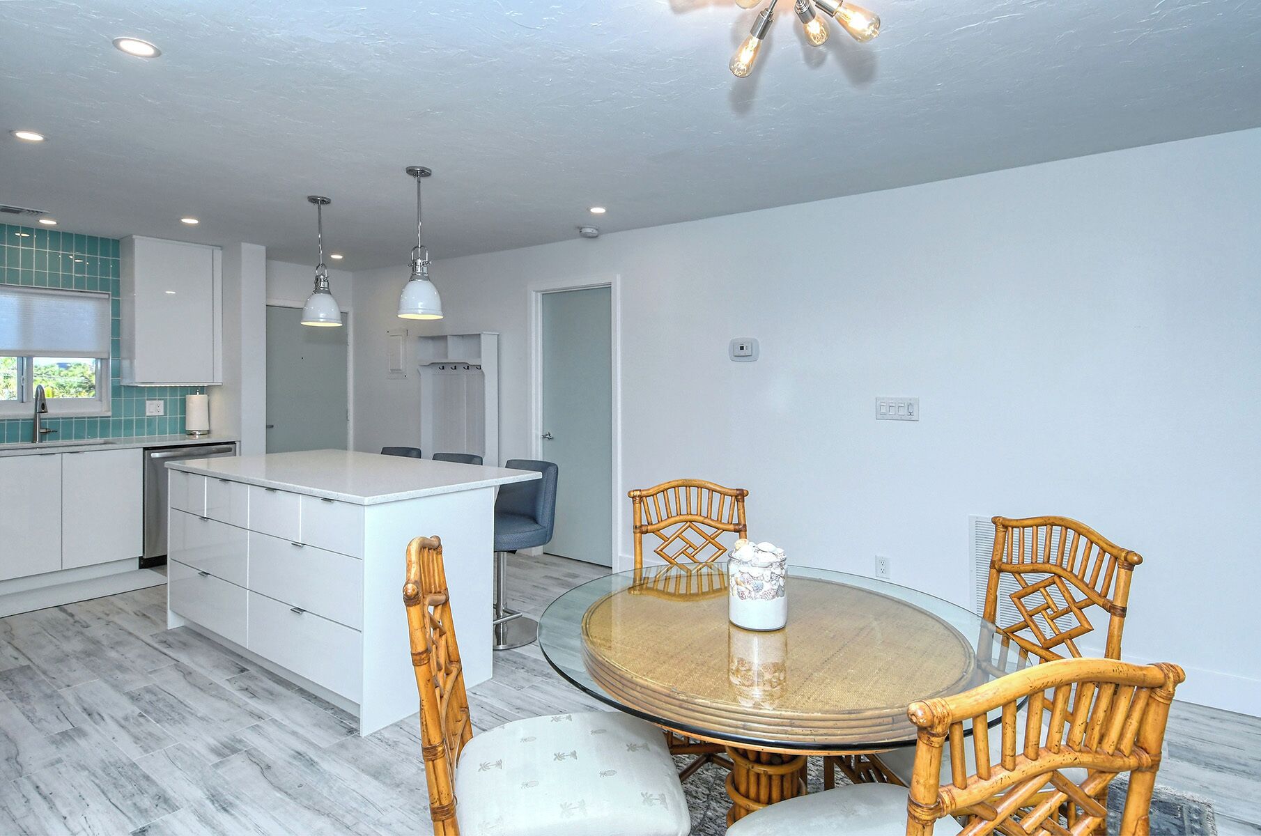 A modern kitchen with white cabinets, a central island, and a dining area with a round glass table and wicker chairs.
