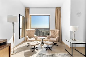 Un salon moderne avec deux fauteuils, une petite table ronde, un lampadaire et une grande fenêtre donnant sur la ville.