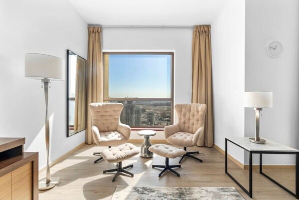 Un salon moderne avec deux fauteuils, une petite table ronde, un lampadaire et une grande fenêtre donnant sur la ville.
