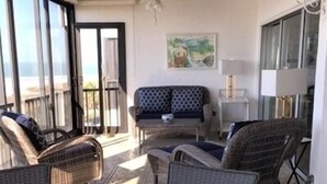 Ein sonnendurchflutetes Zimmer mit einem runden Tisch, Korbstühlen, einer Couch und einem Deckenventilator.