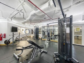 Une salle de sport équipée de divers appareils d’exercice, d’un téléviseur et d’un extincteur.