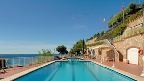 A swimming pool with a clear view of the sea, a stone wall, and flags. - Residence Sant'anna  Three-room Apt  8 Pax Classic (Pietra Ligure)