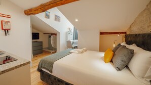 Une chambre avec un grand lit, une poutre en bois au plafond, un bureau avec un ordinateur portable et une chaise.