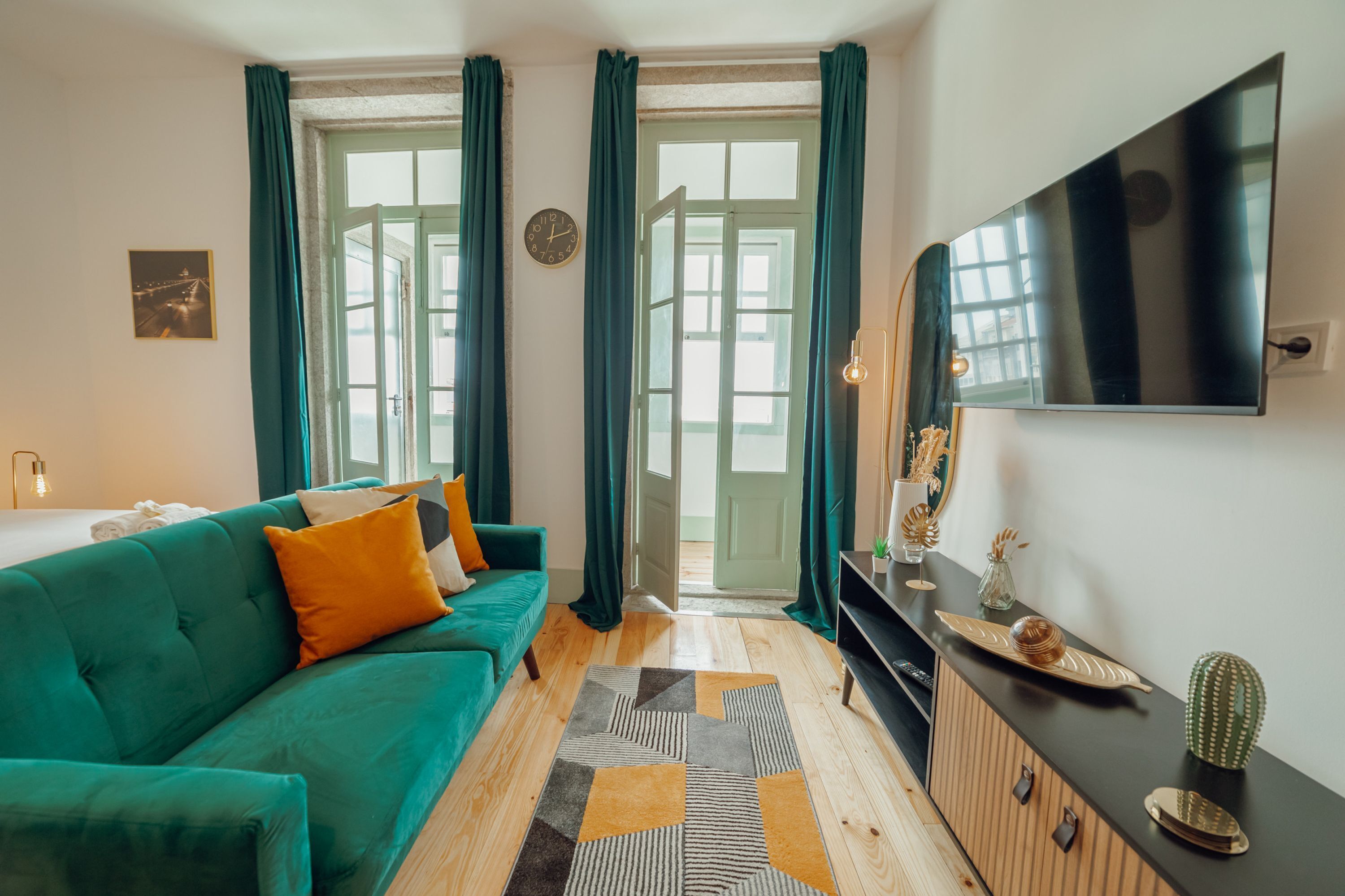Ein modernes Wohnzimmer mit einem türkisfarbenen Sofa, Holzboden, einem Flachbildfernseher und Blick durch eine Glastür.
